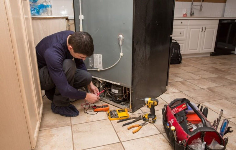 Person repairing a water heater in a kitchen with tools and equipment on the floor.